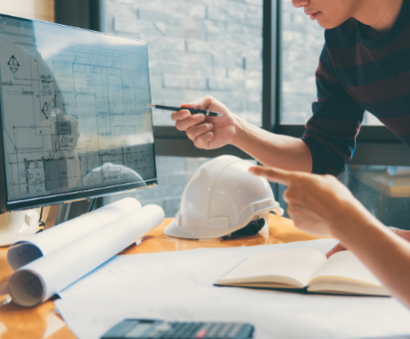 Photo of two architects pointing at building plans on computer screen.
