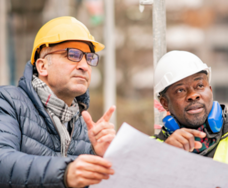 Photo of building engineers with helmets looking at building plans.
