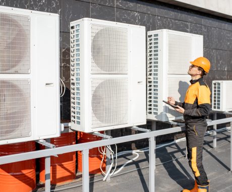 Professional workman in protective clothing adjusting the outdoor unit of the air conditioner or heat pump with digital tablet
