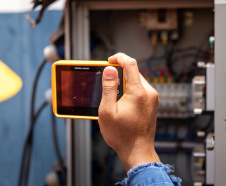An electrician using thermal imager camera device to scanning heat and temperture profile of electric junction box for safety inspection. Industrial working and equipment photo.